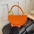 Detailaufnahme einer leuchtend orangefarbenen Satteltasche mit goldenem Griff. - Orange