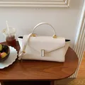 Elegant cream white structured handbag with top handle and gold clasp on a wooden table - Off White