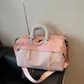 Vue détaillée d'un sac de voyage rose avec poignées grises sur un siège en cuir noir - Rose