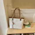 Minimalist beige canvas tote bag with brown trim placed on a wooden shelf next to books - With Charm / Off White