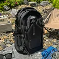 Detail view of black waterproof outdoor hiking backpack placed in a nature camping setting. - Black