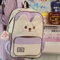 Detailed view of a cute pastel purple and cream cat-themed backpack with a plush charm. - Purple