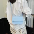 A stylish minimalist light blue small square bag worn as a chic shoulder bag on a white shirt - Blue