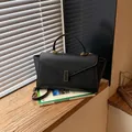 Elegant black pebbled leather handbag with gold buckle on a wooden windowsill - Black