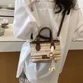 Detailaufnahme einer gewebten Stroh-Eimertasche mit Blumenanhänger und braunem Lederbesatz. - Handgewebt (YM0193) / Gestreift Khaki