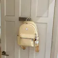 Dettaglio zaino intrecciato crema con tasca a zip appeso a una porta bianca. - Con Ciondolo / Giallo