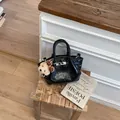 Detailed view of a fashionable black glossy bucket handbag placed on a wooden stool - With Pendant / Black