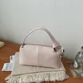 Close-up of a pale pink retro pillow handbag styled on a wooden desk with a textured background - Pink