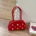 Bolso bandolera rojo retro con lunares apoyado en una pared blanca junto a libros - Rojo