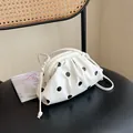 Detail view of a white pleated cloud shoulder bag with black polka dots on a black chair. - Off White