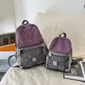Zwei leichte Rucksäcke in Lila und Grau im Set zum Größenvergleich auf einem hellen Sofa. - L / Lila