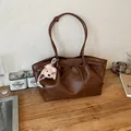 Close-up of brown leather tote bag with bow detail and cute plush puppy charm pendant. - With Charm / Brown