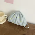 Detailed view of a light blue minimalist cloud bag with yellow polka dots on a wooden table - Blue