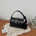 Detail shot of a black glossy retro pillow bag on a wooden table with lifestyle props - Black
