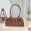 Close-up of a brown polka dot PVC transparent baguette shoulder bag on a white table - Brown