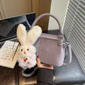 Close-up of a purple small handbag with a cute plush rabbit charm in detail. - With Charm / Deep purple
