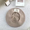 Detailed top-down view of a cozy beige knitted beret with a stylish white letter patch. - 55-60cm / Beige