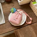 Detail view of a pink mesh drawstring bucket bag on a white plate and wooden table. - With Charm / Pink