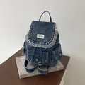 Detailed close-up view of a vintage denim backpack with lace trim placed on an art book - Dark Blue