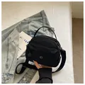 Close-up detail showing the compact black nylon shoulder bag with circular logo design - Black