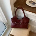 Detail view of a stylish deep red leather tote bag featuring a vintage belt buckle accent - Red