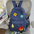 Detail view of a navy blue school backpack with colorful plush flower patches. - With Charm / Blue