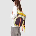 Professional side view of a vibrant color-blocking outdoor hiking backpack worn by a model - Orange Taro Purple