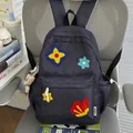 Close-up of a cute navy blue school backpack featuring colorful floral embroidery on a grey chair - With Charm / Black