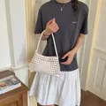 Modèle tenant un sac cabas en cuir tressé blanc dans un décor intérieur minimaliste - Blanc Cassé