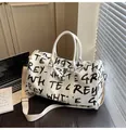 Stylish white graffiti travel duffel bag with black letter print on a desk setting. - White