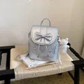 Cute silver bow backpack with dog-themed patches and bear charm displayed on a woven chair. - With Pendant / Silver