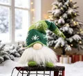 Detail view of a festive green knitted Christmas gnome doll sitting on a red sleigh - Short Leg with LED / Green