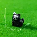 Cute Halloween miniature black cat figurine with skull mask on green grass landscape - Raising Paw Style