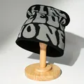 Schwarze Strickmütze mit grauen Buchstabenmustern auf einem Holzständer für den Winter. - Schwarz und Grau