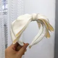 Primo piano dettagliato di un cerchietto in raso crema con fiocco elegante e trama raffinata - Modello a fiocco / Bianco latte