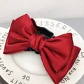 Primo piano di un grande fermaglio per capelli con fiocco in raso rosso su un piatto bianco decorato - Borgogna