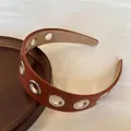 Dettaglio di un cerchietto in pelle marrone con occhielli in metallo argentato. - Marrone