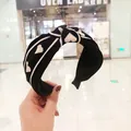 Dettaglio ravvicinato di una fascia larga in maglia nera con cuori bianchi e design a nodo chic - Cuore Nero