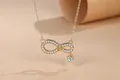 Close-up of gold infinity necklace with micro-pave stones and a heart-shaped charm. - Gold
