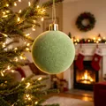 Elegante pallina di Natale floccata in velluto verde salvia su un albero illuminato - Verde matcha