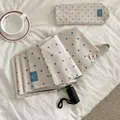 Beigefarbener Faltschirm mit blauen Punkten und passender Hülle auf weißem Stoffbett - Beige (Automatisch)