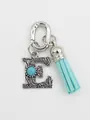 Detailed macro view of ethnic style silver letter E charm with turquoise stone and blue tassel - Letter E
