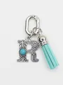 Close-up of an ethnic silver letter R bag charm featuring turquoise inlay and a blue suede tassel - Letter R