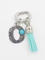 Close-up of bohemian letter O charm with turquoise bead and light blue tassel ornament. - Letter O