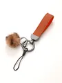 Close-up of a stylish orange leather keychain with a plush brown pom pom and grey metal ring - Keychain Pendant / Orange