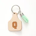 Detail of faux leather cow tag keychain featuring letter Q and soft green tassel - Letter Q Style (20447)