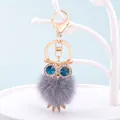 Eulen-Schlüsselanhänger aus Kunstfell mit blauen Strassaugen und goldenem Metallclip - Großaugen Eule - Grau