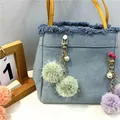 Detalle de un lindo llavero de pompones con perlas colgado de un elegante bolso de mezclilla - Verde Claro