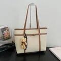 Elegant cream textured tote bag featuring brown straps and a cute plush bear charm - White
