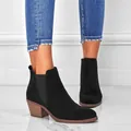 Close-up of black suede ankle boots with chunky wood-textured heels worn with blue jeans. - Black